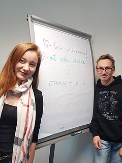 Zwei Studierende vor einem Flipchart. Auf diesen steht "Herzlich willkommen"