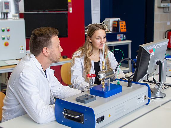 Labormeister erklärt einer Studierenden den Versuchsaufbau der Wärmeübertragung in Fluiden.uiden