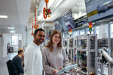 Two students program a robot in the digital factory.