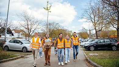 Studierende tragen Kirschbaum über Parkplatz