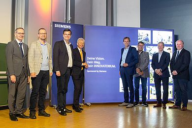 Vertreter von Hochschule und Siemens stehen vor der beleuchteten LED-Wand