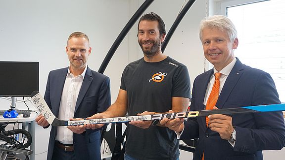 Drei Männer halten einen Eishockeyschläger