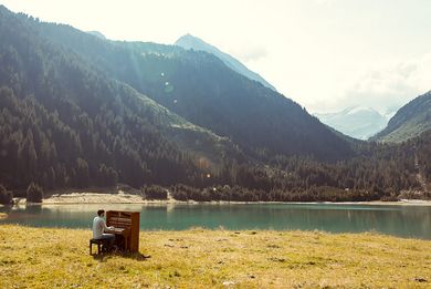 Klavier auf einer Wiese, im Hintergund Alpen