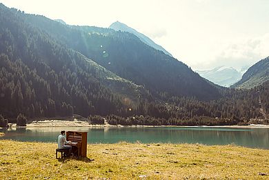 Klavier auf einer Wiese, im Hintergund Alpen