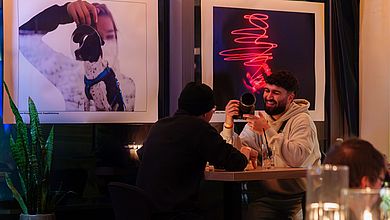 Studierende unetrhalten sich, im Hintergrund zwei Fotos