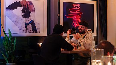 Studierende unetrhalten sich, im Hintergrund zwei Fotos