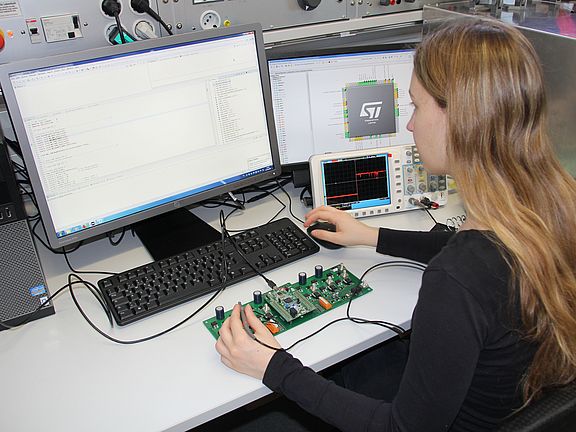 Studentin sitzt im Labor und misst an einer Platine