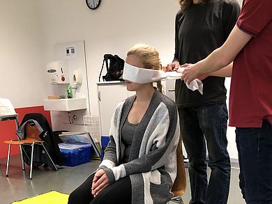 Studierende binden Studentin Augen zu