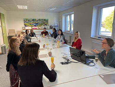 Menschen sitzen an einem langen Tisch. Vor ihnen stehen Sektgläser, gefüllt mit Wasser, O-Saft oder Sekt