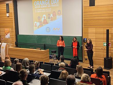 Drei Frauen stehen in einem Hörsaal vor Menschen