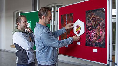 Zwei Männer stehen vor einer Pinnwand mit Bilder