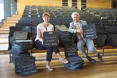 zwei Personen präsentieren Sitzkissen in einem Hörsaal