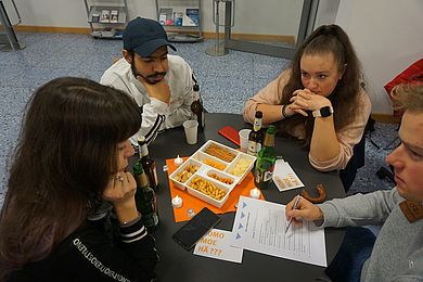 Vier Personen sitzen um einen Tisch und schauen auf ein Blatt Papier