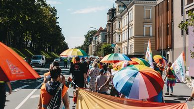 Menschen laufen am Rand einer Straße, viele haben Regenbogenschirme aufgespannt