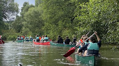 Mädchen sitzen in mehren Kanus und paddeln auf einem kleinen Fluss