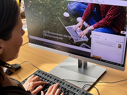 Persone vor Computer, Chatfenster ist auf dem Monitor zu sehen
