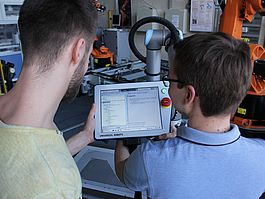 Zwei Studenten steuern den Industrie-Roboter mit einem Tablet.