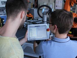 Zwei Studenten steuern den Industrie-Roboter mit einem Tablet.