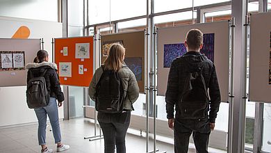 Junge Menschen schauen Bilder auf Pinnwänden an