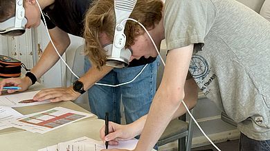 Theorie trifft Praxis: Noch mit aufgesetzter Apple Vision Pro halten zwei Schüler ihre Beobachtungen auf dem Arbeitsblatt fest