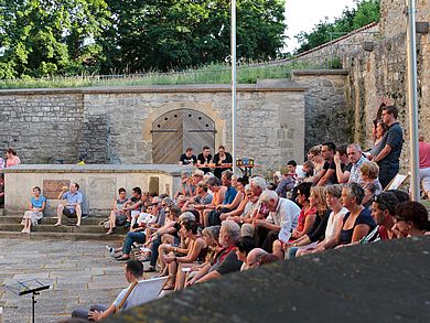 Publikum sitzt auf den Stufen des Vorplatzes