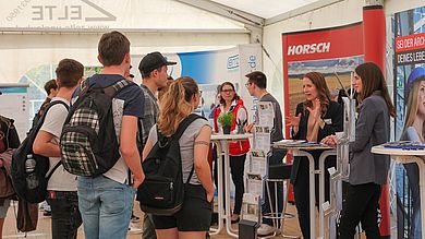 Studierende informieren sie bei einem Messestand