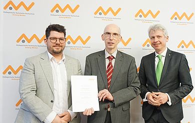 Drei Männer posieren mit Urkunde vor einer Logowand