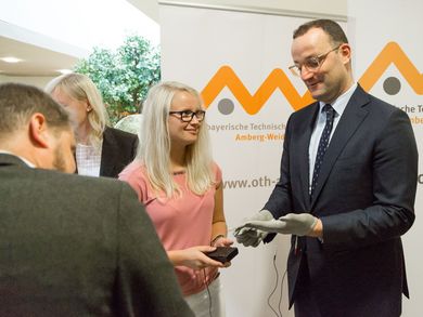 Sabrina Reiml, OTH Amberg-Weiden, erläutert Bundesminister Jens Spahn die Funktionsweise des Tremor-Handschuhs. 