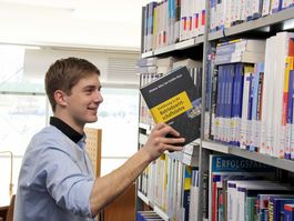 Student nimmt Buch aus dem Regal in der Bibliothek der Hochschule