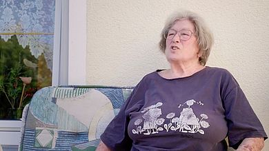 Ältere Frau sitzt auf Bank und erzählt