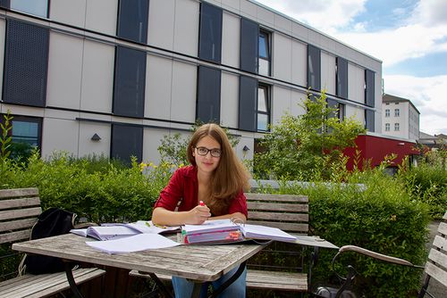 Studentin Julia Eberlein sitzt auf einer Bank vor dem Studentenwohnheim