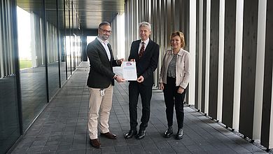 Drei Personen posieren mit einer Urkunde