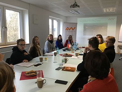 Etwa 10 Personen sitzen um einen großen Konferenztisch
