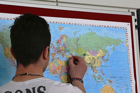 Junger Mann pinnt eine Stecknadel in sein Heimatland