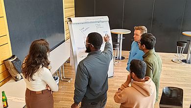 Fünf Leute stehen vor einem Flipchart