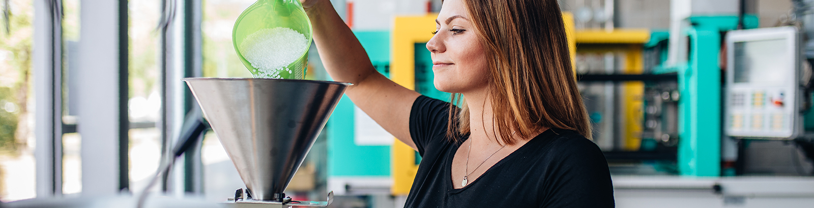 Studentin füllt Kunststoffgranulat im Labor für Kunststofftechnik in einen Trichter.